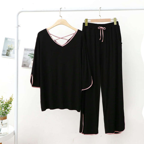 A black colored PJ set with pink lace v-neck and palazzo pants, hanging on a hanger against a white background, with books and a potted plant in the background.