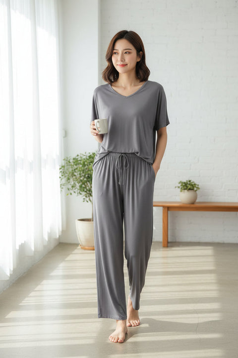 A grey V-neck shirt with half sleeves and a matching pair of palazzo trousers, displayed on a hanger and a flat surface respectively.