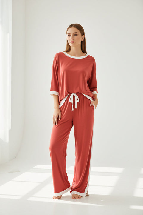 A red sleeveless pajama night suit with a round neckline and white accents, displayed on a hanger and being adjusted by a hand.