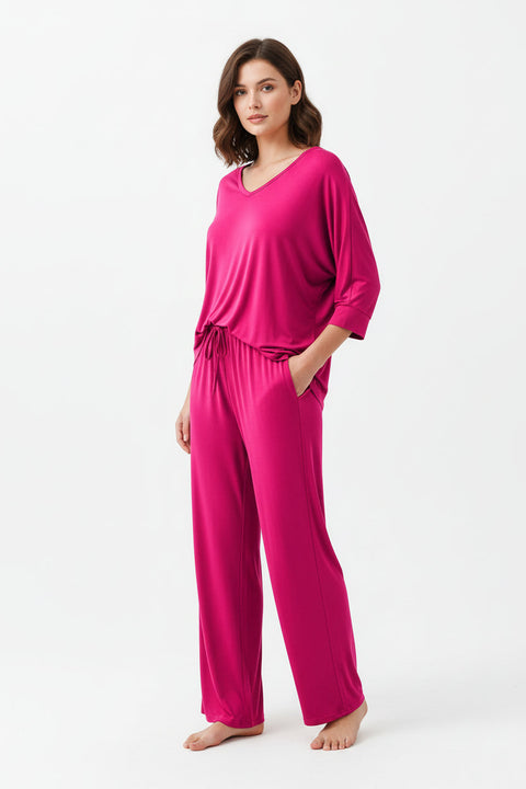 A shocking pink V-neck with palazzo style pajama full sleeves suit hanging on a hanger, with a person's hand adjusting the fabric.