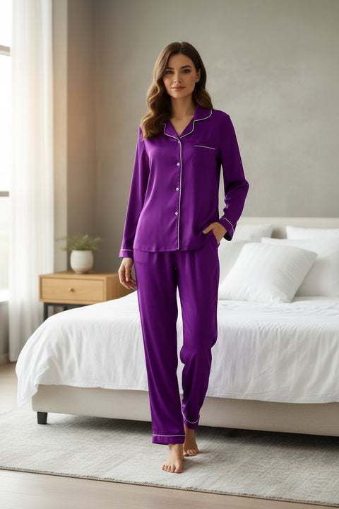 Purple satin pajama set on a white bed with a wooden hanger.