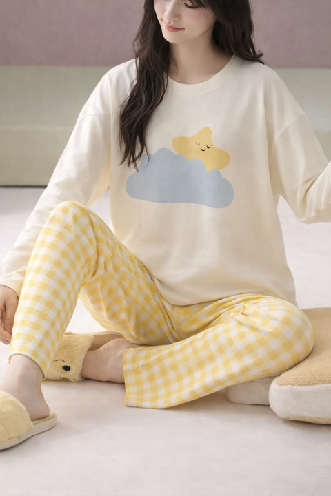 Woman wearing a cream-colored top with a cloud and star design and yellow checkered pants, sitting on a couch.