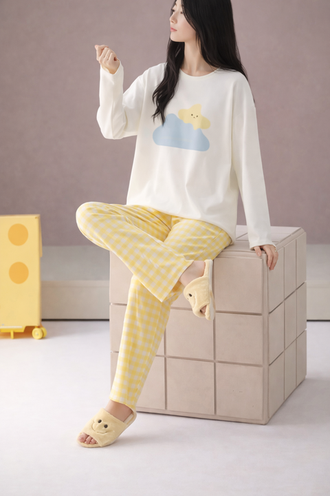 Woman wearing a white long-sleeve top with a cloud design and yellow checkered pants, sitting on a beige cube.