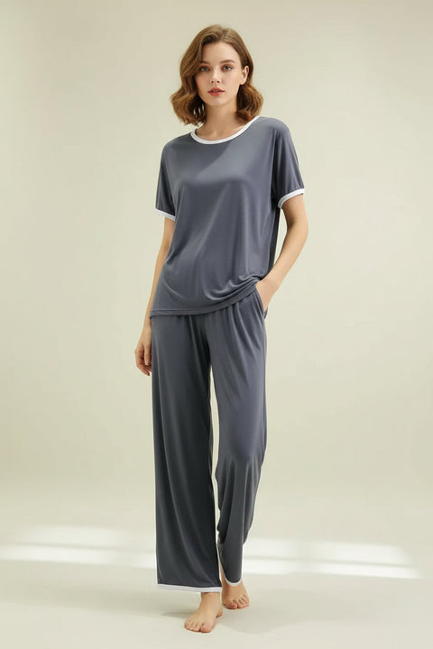 A plain grey round neck half sleeves top and flapper trousers hanging on a hanger. A person is adjusting the sleeve of the top by pulling it downwards.