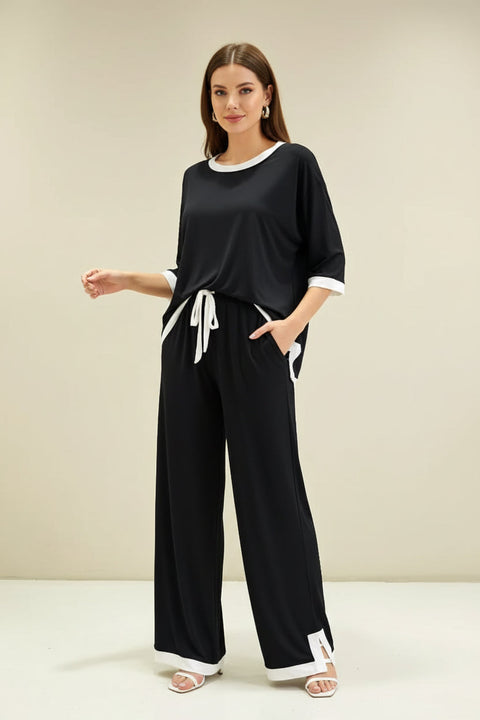 A black and white round neck flapper pajama night suit hanging on a hanger, with a person's hand pointing to the white collar and sleeve detail.