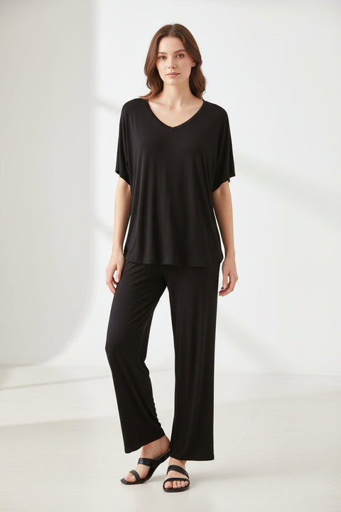 A black V-neck shirt with half sleeves and a pair of matching palazzo trousers displayed on a hanger, with a hand adjusting the shirt.