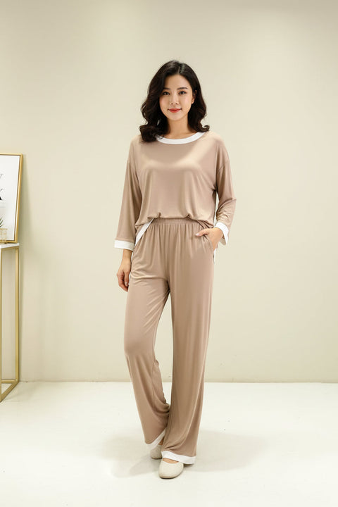 A beige with white round neck flapper pajama night suit displayed on a hanger, with a person's hand adjusting the fabric.